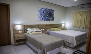 a bedroom with two beds and a painting on the wall at Hotel Baeza in Goiatuba
