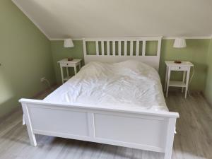 a white bed in a room with two tables at Domek wakacyjny nad jeziorem Gowidlińskim in Podiazy
