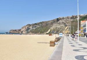 een strand met banken en een berg bij Blue Sea Nazaré Apartament in Nazaré