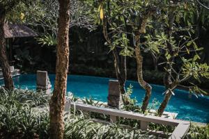 a white bench next to a pool with trees at Kharista Villas & Retreat by Ekosistem in Canggu