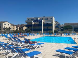 basen z niebieskimi krzesłami i leżącymi na nich ludźmi w obiekcie Appartement COSY avec piscine, accès direct plage w mieście Lacanau-Océan