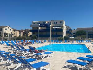 una piscina con sedie blu e persone sdraiate su di esse di Appartement COSY avec piscine, accès direct plage a Lacanau-Océan