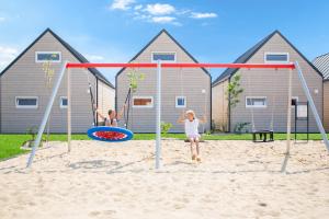 two children playing on a swing set in the sand at Resort Za Lasem in Jarosławiec