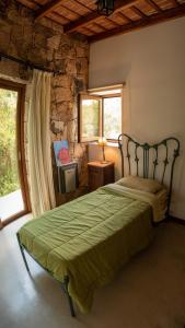 a bedroom with a green bed with a stone wall at Costas del Cuniputu - Casa de Campo in Capilla del Monte