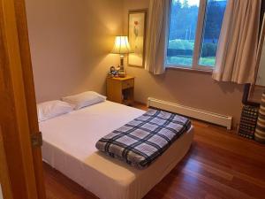 a bedroom with a bed with a lamp and a window at Metchosin Beach House in Victoria