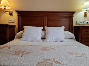 1 cama con almohadas blancas y cabecero de madera en Hotel Plateros, en Córdoba