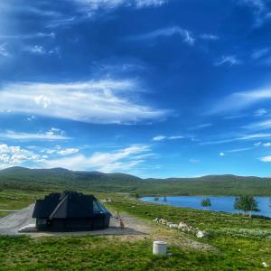 une grande tente noire dans un champ à côté d'un lac dans l'établissement Arctic Land Adventure Glass Igloos, à Kilpisjärvi