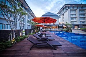 eine Reihe von Liegestühlen mit Sonnenschirmen neben einem Pool in der Unterkunft HARRIS Hotel & Conventions Malang in Malang