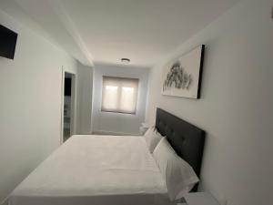 Dormitorio blanco con cama con sábanas blancas y ventana en apartamento isabel en Ardales