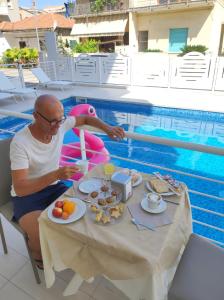 un homme assis à une table avec de la nourriture à côté d'une piscine dans l'établissement Nuovo HOTEL SETTIBI 20m dalla spiaggia, à Giulianova
