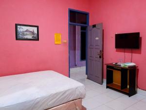 Dormitorio con pared de color rosa, cama y TV en Hotel Rosichan Bau Bau Mitra RedDoorz en Baubau