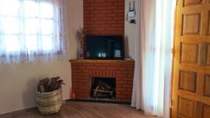 uma sala de estar com uma lareira de tijolos e uma televisão em Aconchegante chale com Wi Fi em Sapucai Mirim MG em Gonçalves