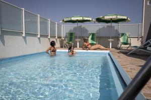 Três raparigas estão sentadas numa piscina. em Amadei Hotel Figaro & Apartments em Pesaro