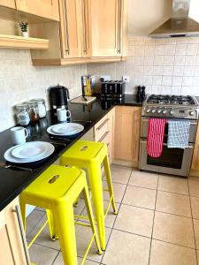 a kitchen with two yellow stools and a stove at NEW! Luxury YELLOW HOUSE Bright Modern Detatched Home with PRIVATE PARKING, NETFLIX Close Luton, M1, and AIRPORT Ideal for Families, Professionals, Consultants, LONGER STAY OPTIONS in Caddington