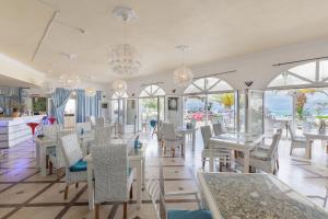 a restaurant with white tables and chairs and windows at Aphrodite Beachfront Hotel by Konnect, Roda in Roda