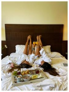 two women laying on a bed with a tray of food at Hotel Albaida Nature in Mazagón