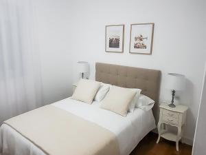 1 cama blanca con almohadas blancas y 2 lámparas en una mesa en Piso en Muxía con magníficas vistas al mar, en Muxía