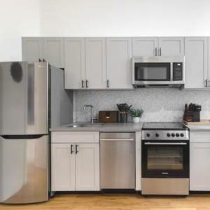 una cocina con armarios blancos y electrodomésticos de acero inoxidable en Modern Holiday Apartment with Strategic Location in New York, en Nueva York