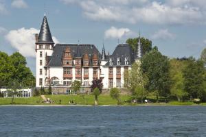 ein großes weißes Gebäude mit einem schwarzen Dach neben einem Wasserkörper in der Unterkunft Seehotel Schloss Klink in Klink