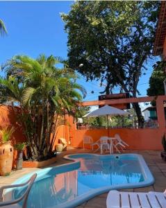 uma piscina com cadeiras e um guarda-sol e palmeiras em Pousada do Carlos em Arraial d'Ajuda