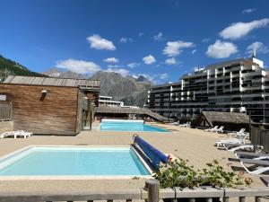 a swimming pool with chairs and a building at Studio Puy Saint Vincent 1600 aux pieds des pistes in Puy-Saint-Vincent
