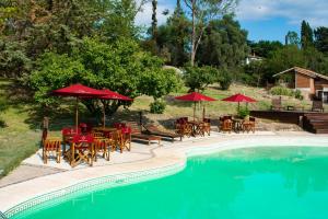 a pool with tables and chairs and red umbrellas at Capilla del Lago in Villa Carlos Paz