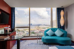 a room with a blue chair and a desk and a large window at Zhuhai Charming Holiday Hotel-Free Welcome Fruit Plate in Zhuhai