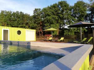 a pool with a yellow building and chairs and umbrellas at DES BRANCHES & VOUS in Châteauneuf-sur-Isère