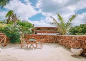 un patio con parete in pietra, tavolo e sedia di Tropicana Garden a Kendwa
