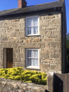 an old stone house with two windows and bushes at 3 bedroom Grade II Listed Holiday Cottage in Saint Erth