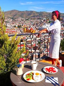 a woman standing on a balcony with plates of food at Casa Rofo in Guanajuato
