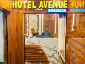 a man is standing behind a hotelagencyagency ape rooms at HOTEL AVENUE AC ROOMS in Ahmedabad