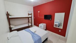 Habitación pequeña con cama y pared roja. en Xodó do Peró Hostel, en Cabo Frío