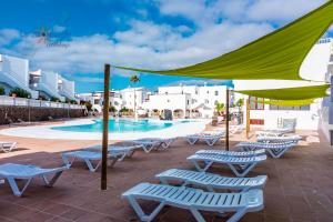 basen z leżakami i zielonym parasolem w obiekcie Vivienda Vacacional Buganvillas w Costa Teguise