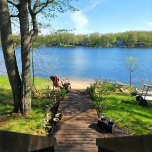 a walkway next to a lake with a tree at Lake Front Cottage on Private All-Sports Lake. in Le Roy