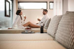 a man and woman sitting on a bed drinking wine at Stoa - Elegant & Romantic Guest House - "Adults only" in San Vigilio Di Marebbe