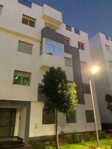 un bâtiment blanc avec un arbre devant lui dans l'établissement Résidence Le joyau de la mer Plage Des Nations, à Sidi Bouqnadel