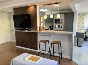 eine Küche mit einer Bar mit Hockern und einem TV in der Unterkunft Apartamento Decorado Coral in Balneário Camboriú