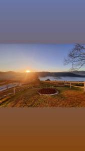 a sunset over a field with a fence and a lake at Pousada Mirante de Minas in Extrema