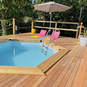 einen Pool mit zwei Stühlen und einem Sonnenschirm auf einer Holzterrasse in der Unterkunft Les Vanniers: Papaye - KARITÉ in Baie-Mahault