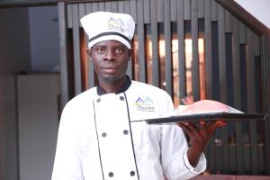 um chef segurando um prato com um bolo sobre ele em Pals Inn em Busia