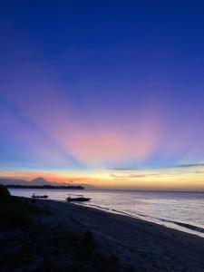 a sunset on a beach with boats in the water at Meno Madia Bungalows in Gili Meno