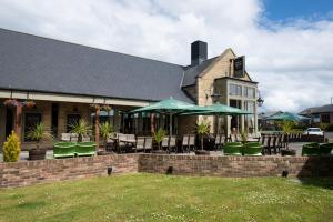 a building with tables and chairs and green umbrellas at The Hog's Head Inn - The Inn Collection Group in Alnwick