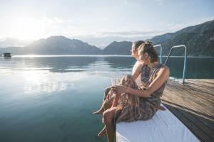 two women sitting on a dock near the water at Hotel Das Zeit in Lenzing