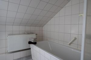 Baño de azulejos blancos con bañera y radiador en Gästehaus Dresden - Alte Schule Gohlis en Dresden