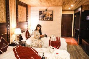 une femme assise sur un lit dans une chambre d'hôtel dans l'établissement Sapa Elegance Hotel, à Sa Pa