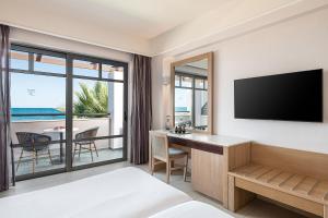 a hotel room with a bedroom with a desk and a television at Porto Platanias Beach Resort & Spa in Plataniás
