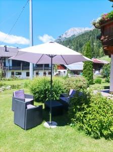 a table and chairs under an umbrella in the grass at Appartamenti Soravia in Sappada