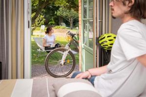 uma mulher sentada num alpendre com uma bicicleta lá fora em Logis Auberge De La Sélune em Ducey