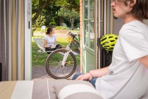 une femme assise sur une terrasse couverte avec un vélo à l'extérieur dans l'établissement Logis Auberge De La Sélune, à Ducey